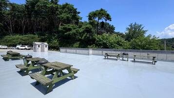 An outdoor seating area with picnic tables and benches, surrounded by trees and a clear sky.