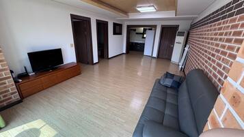 A spacious living room with a flat-screen TV, a sofa, and a brick wall.