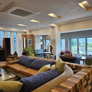 A modern living room with a sectional sofa, a brick accent wall, and large windows offering a view of the outdoors. - Hwimok Art Resort (Buan)