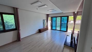 A spacious room with a large sliding glass door leading to an outdoor area, a wooden bench, and a small table with a TV.