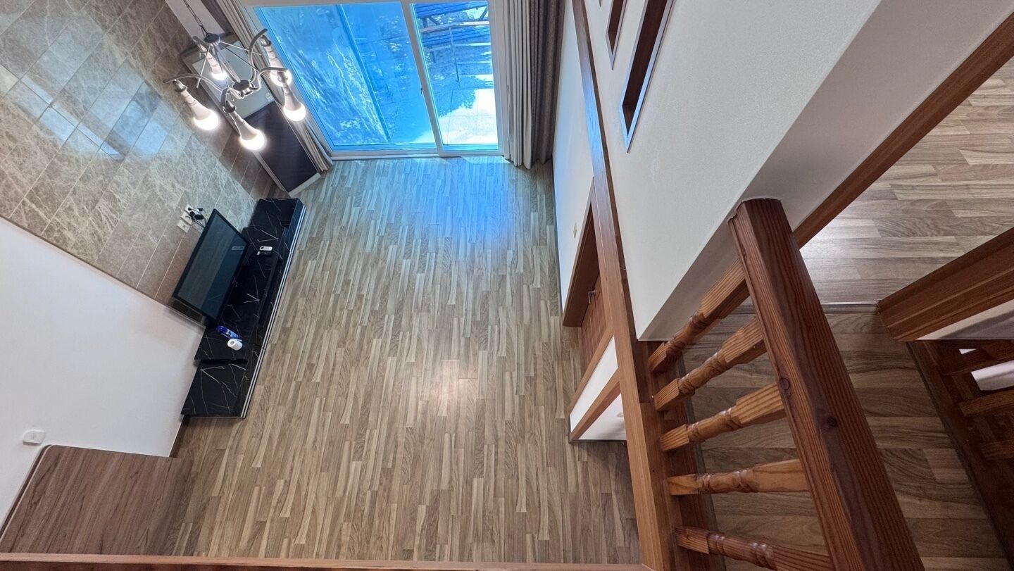 Una escalera conduce a una habitación con piso de madera, un televisor y vistas al exterior.