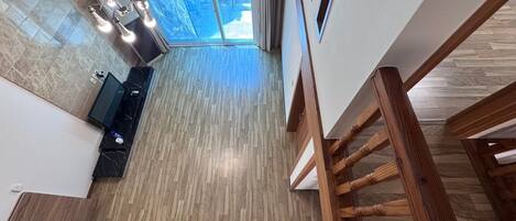 Una escalera conduce a una habitación con piso de madera, un televisor y vistas al exterior.
