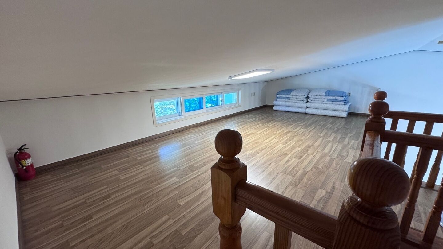 An attic bedroom with wooden flooring, a fire extinguisher, a wooden railing, and a stack of folded towels.