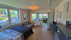 A bedroom with two beds, a desk, and a view of the parking area.