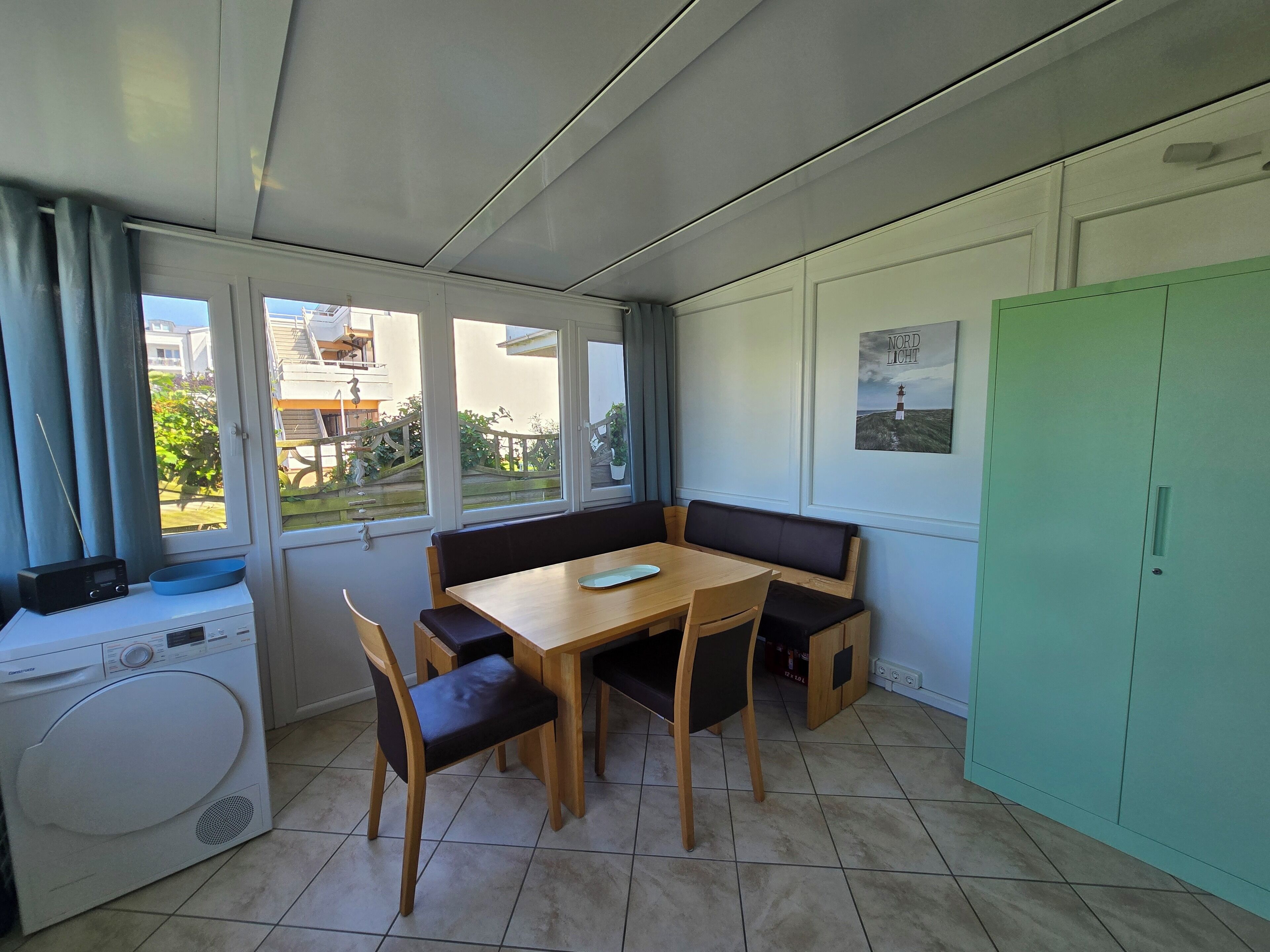Una habitación compacta con una mesa de comedor, bancos, lavadora y un armario verde.