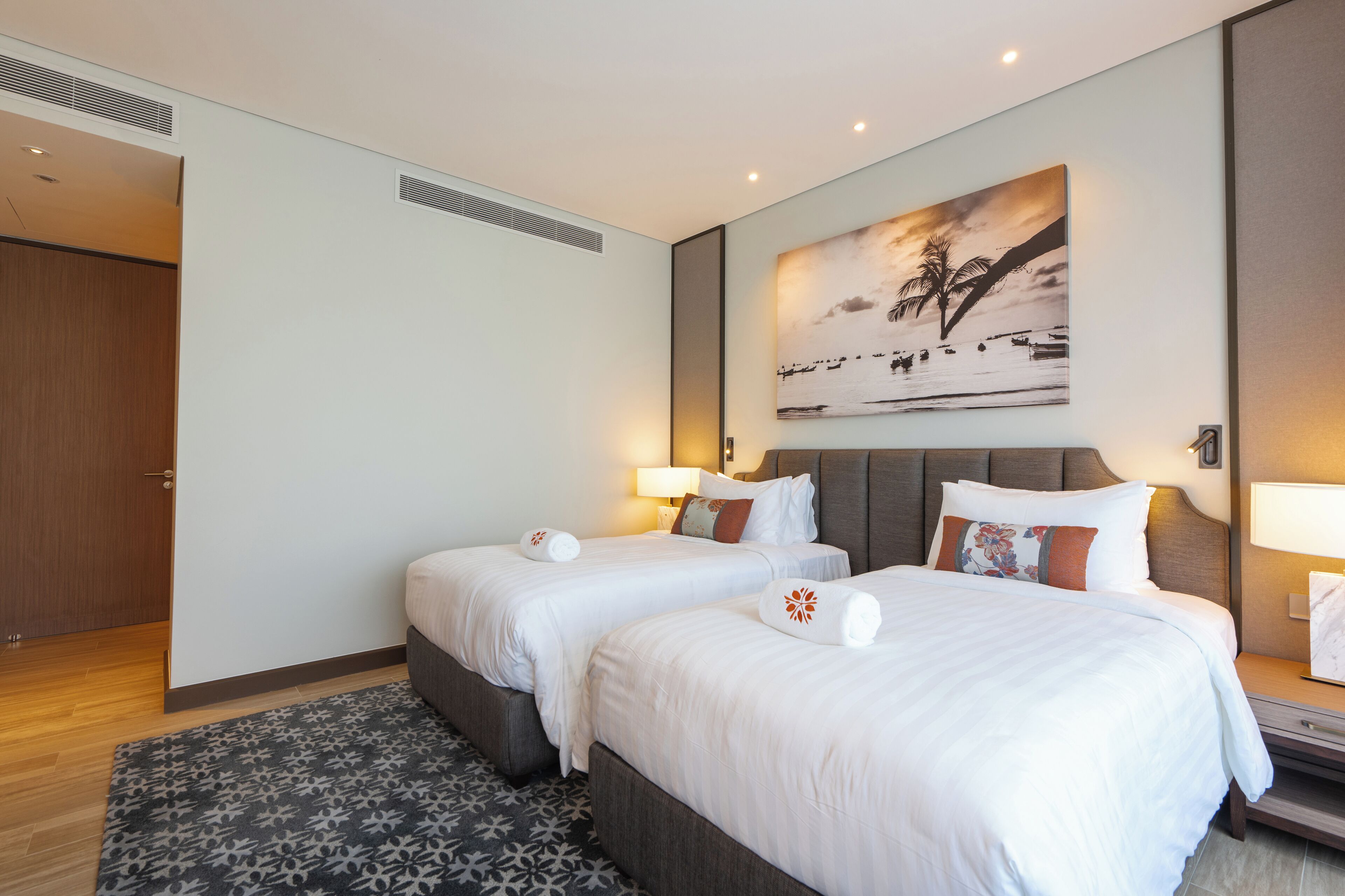 A hotel room with two beds, a large painting on the wall, and a wooden door.