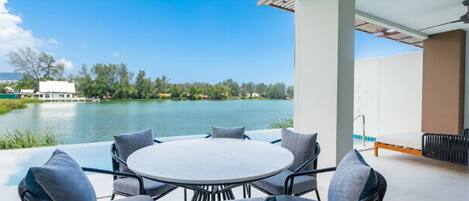 Un patio con una mesa redonda y sillas, con vista a un cuerpo de agua y vegetación.