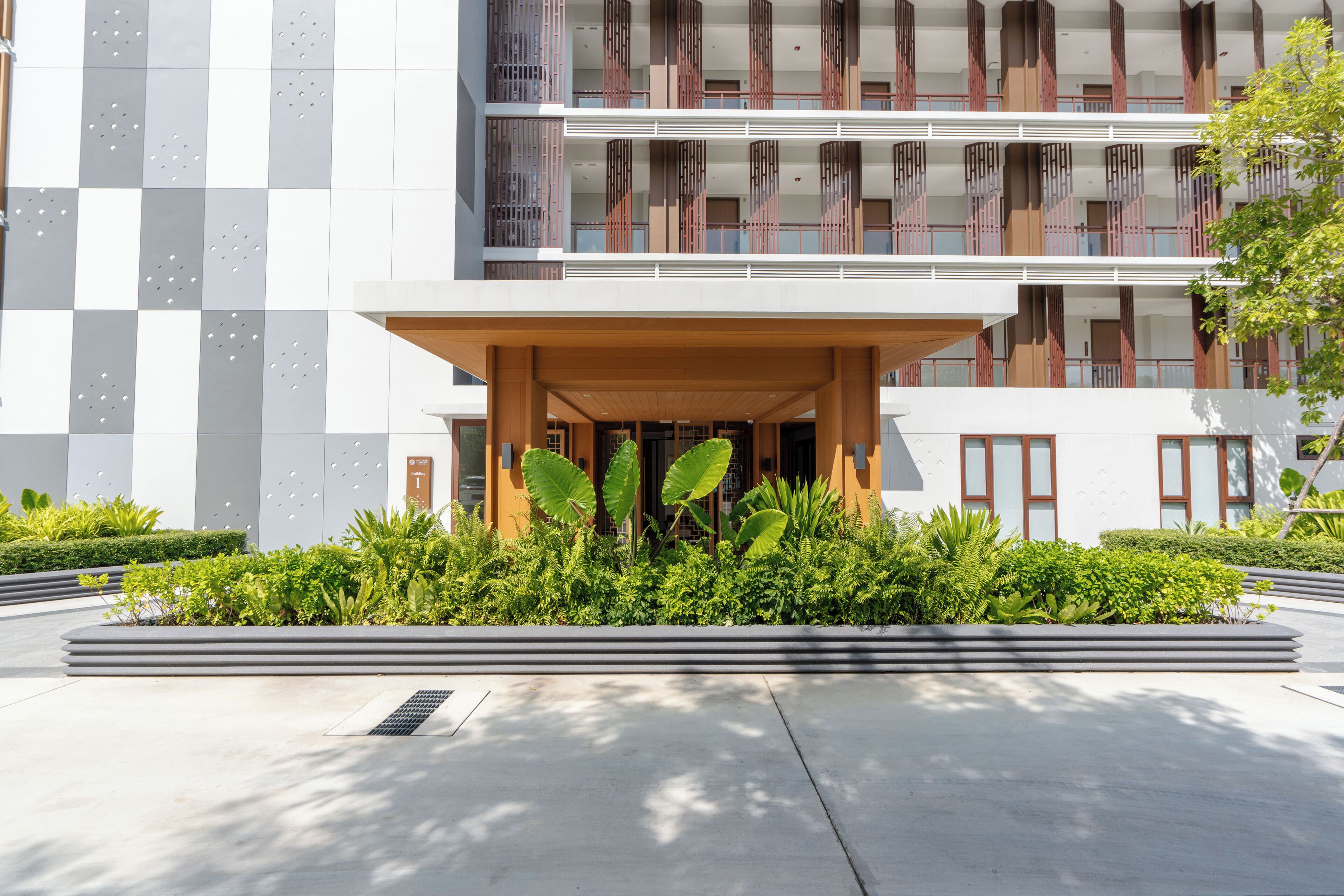 A modern building with a checkered facade, a central entrance with a wooden canopy, and a landscaped garden area.