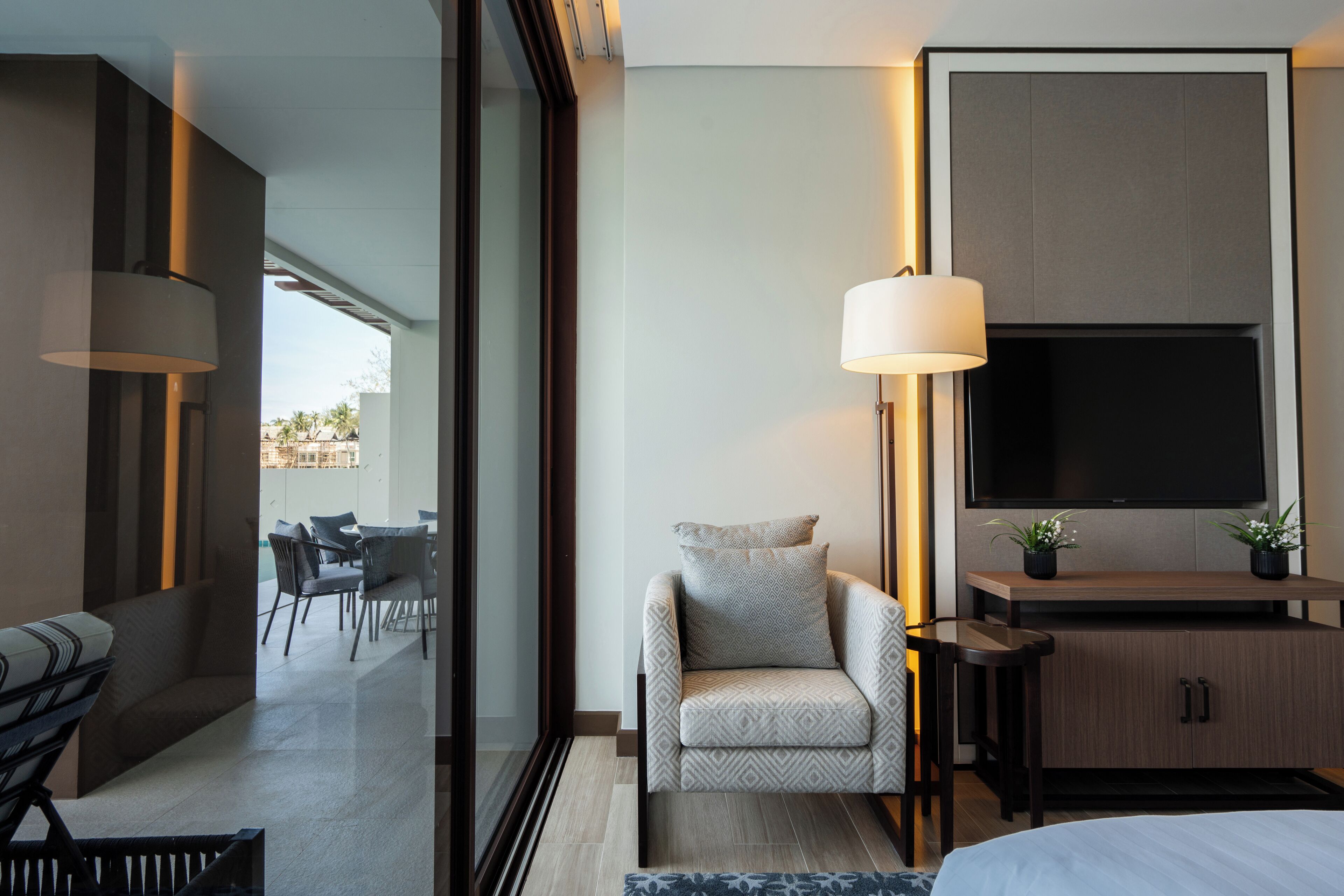 A modern hotel room with a sofa, a chair, a TV, and a desk.