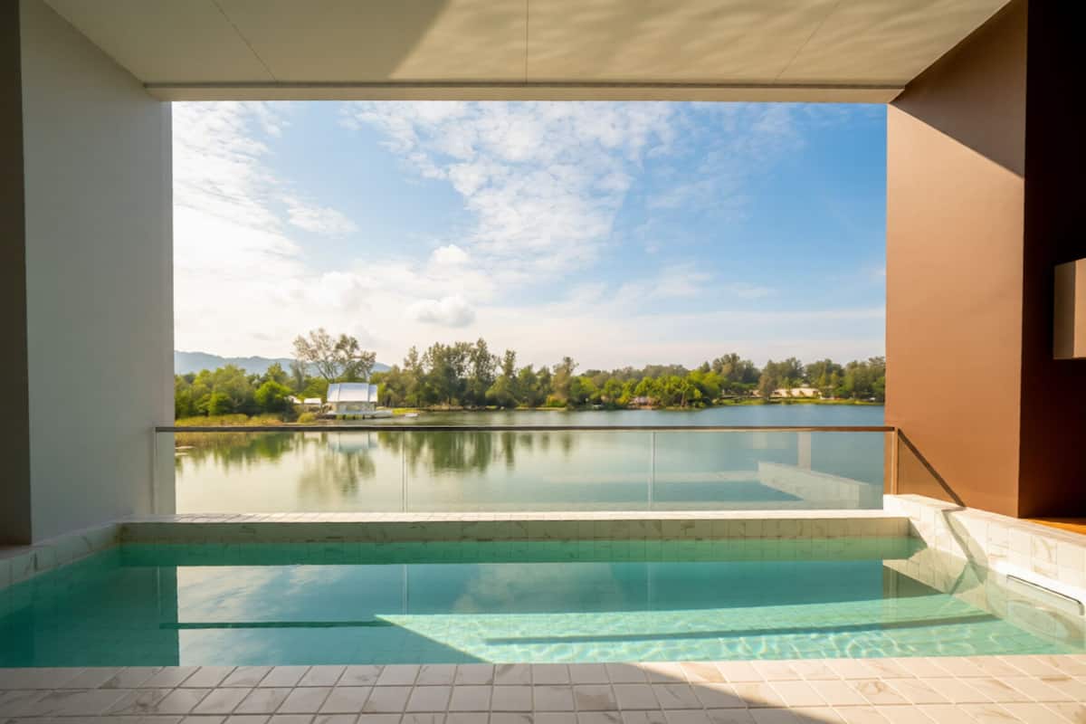 A swimming pool with clear water, surrounded by a tiled floor and walls, with a view of a lake and trees in the background.