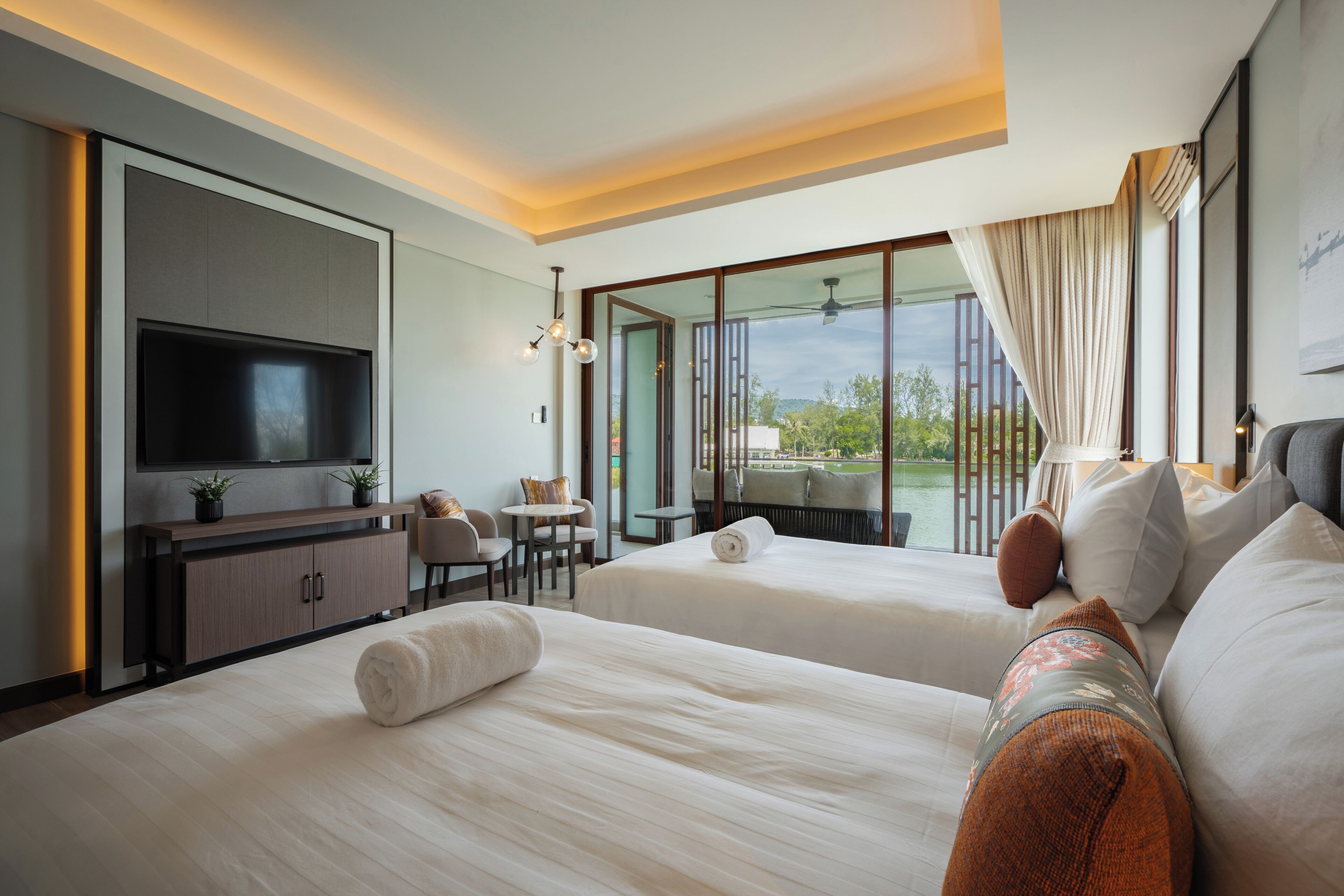 A hotel room with two beds, a TV, a desk, and a view of the outdoors.