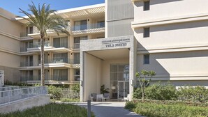 Un hotel moderno con entrada central, varios balcones y un jardín ajardinado.