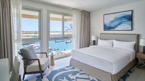 Habitación de hotel con una cama grande, una silla, una mesita y vista a un puerto deportivo.