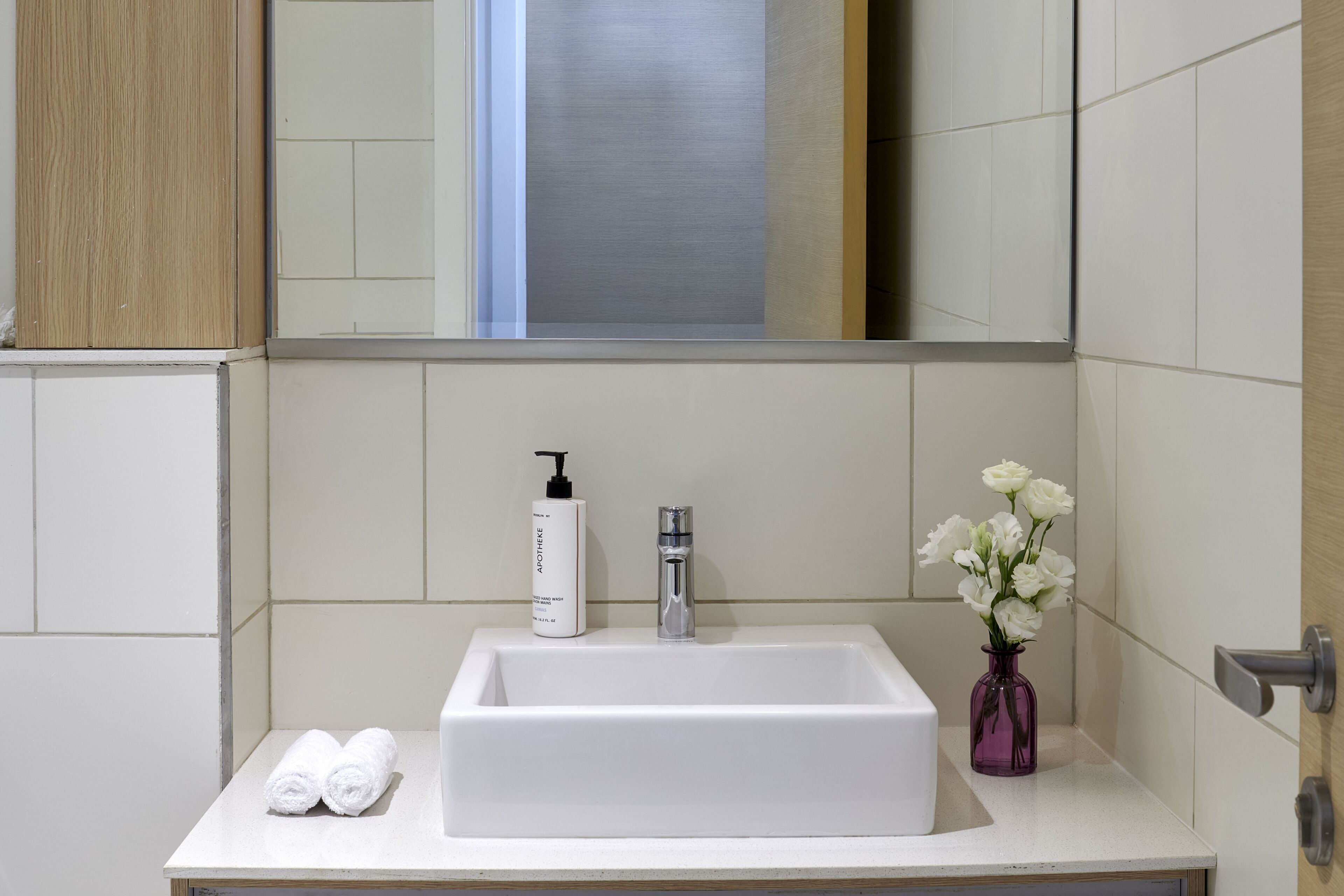 Een badkamer met een wit wastafel, een zeepdispenser, een waterkraan, een spiegel en een vaas met witte bloemen.