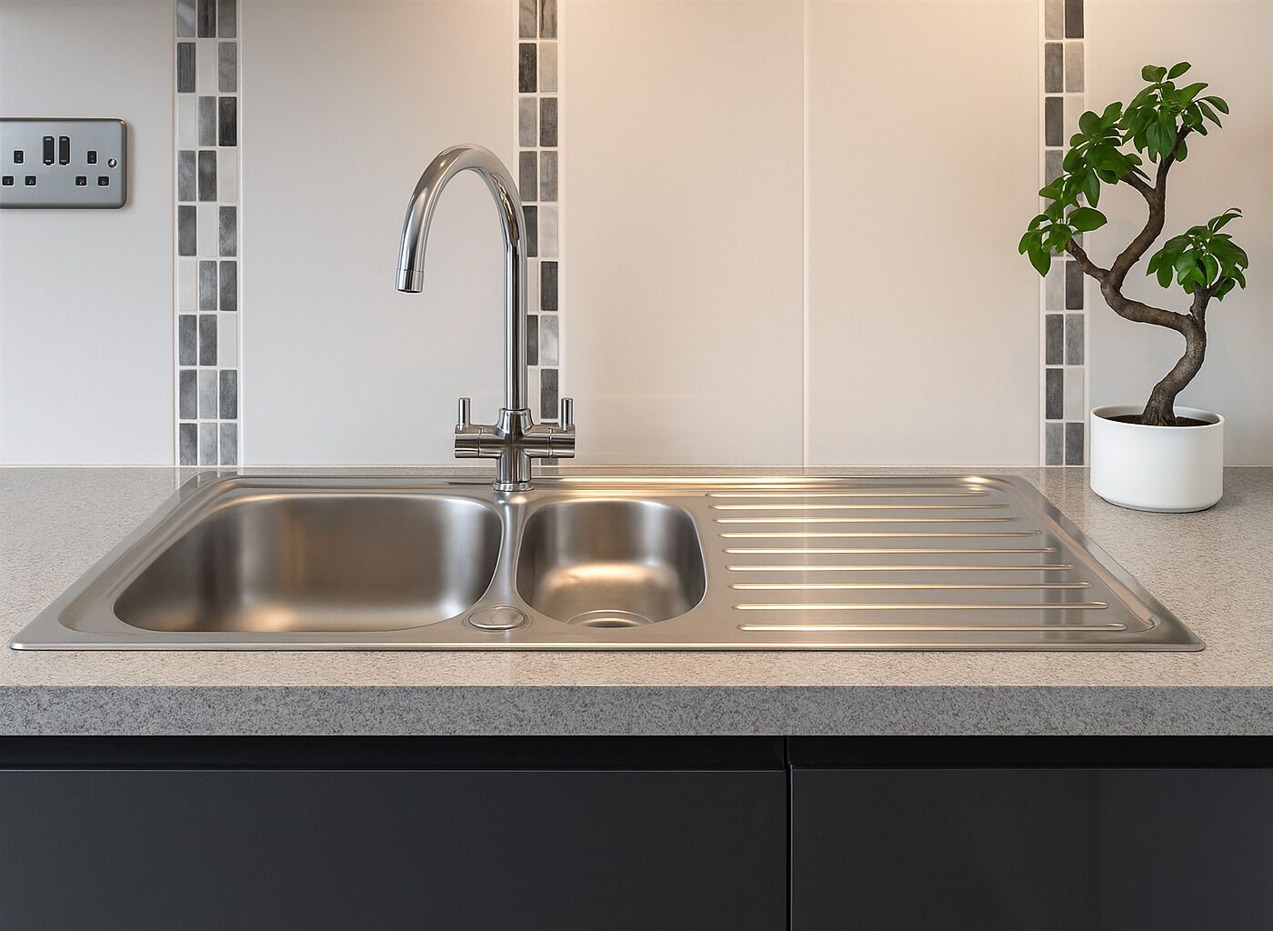 Una cocina moderna con un lavamanos de acero inoxidable, salpicadero con mosaicos y una planta en maceta.