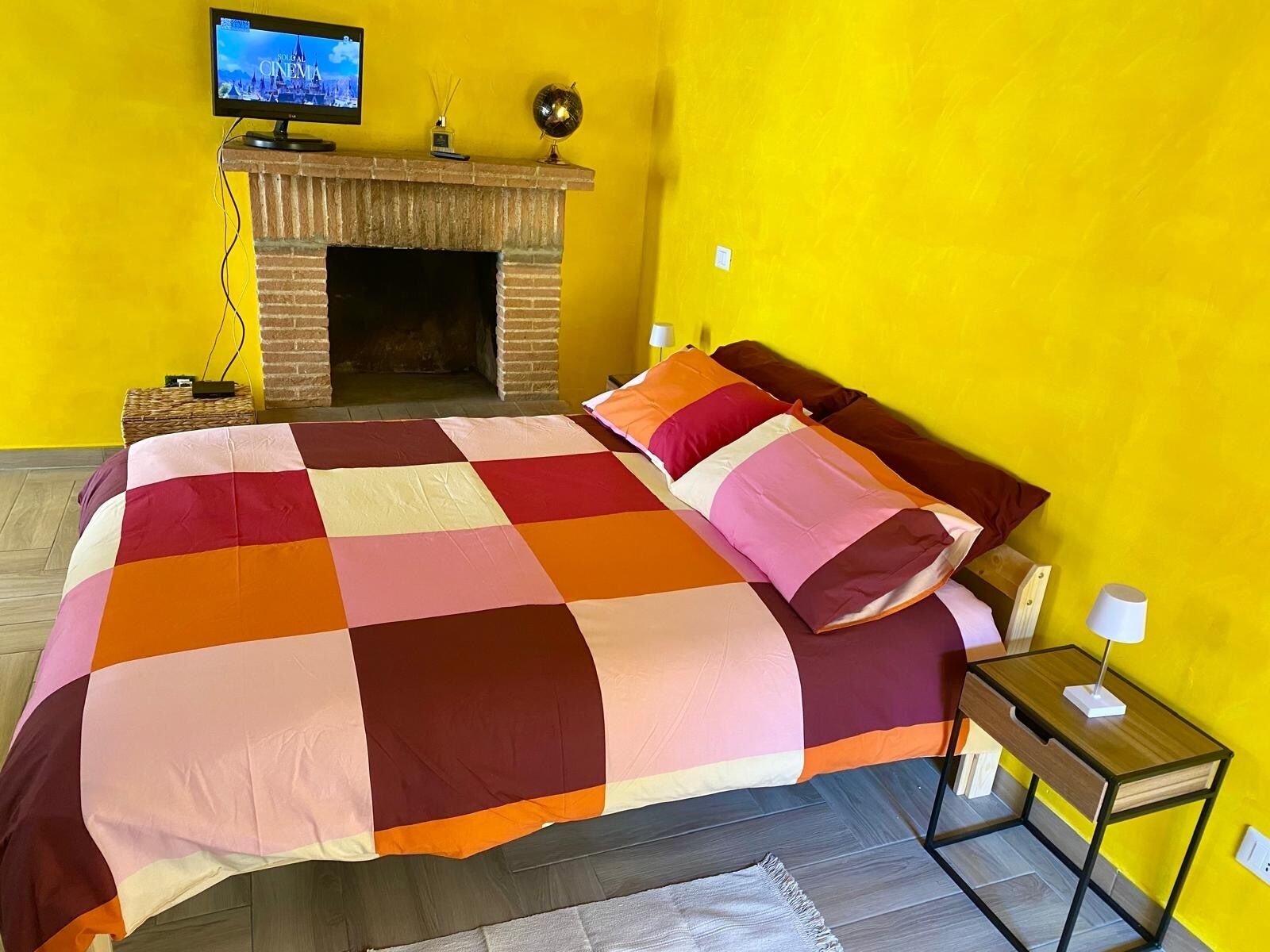 Une chambre à coucher avec un grand lit, une cheminée, un téléviseur posé sur un meuble et une petite table avec une lampe.