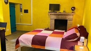 Quarto com cama, lareira, televisão e escrivaninha.