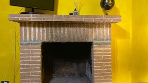 Lareira de tijolos com televisão de tela plana em cima, um globo decorativo e um vaso com raminhos na mantelpiece.