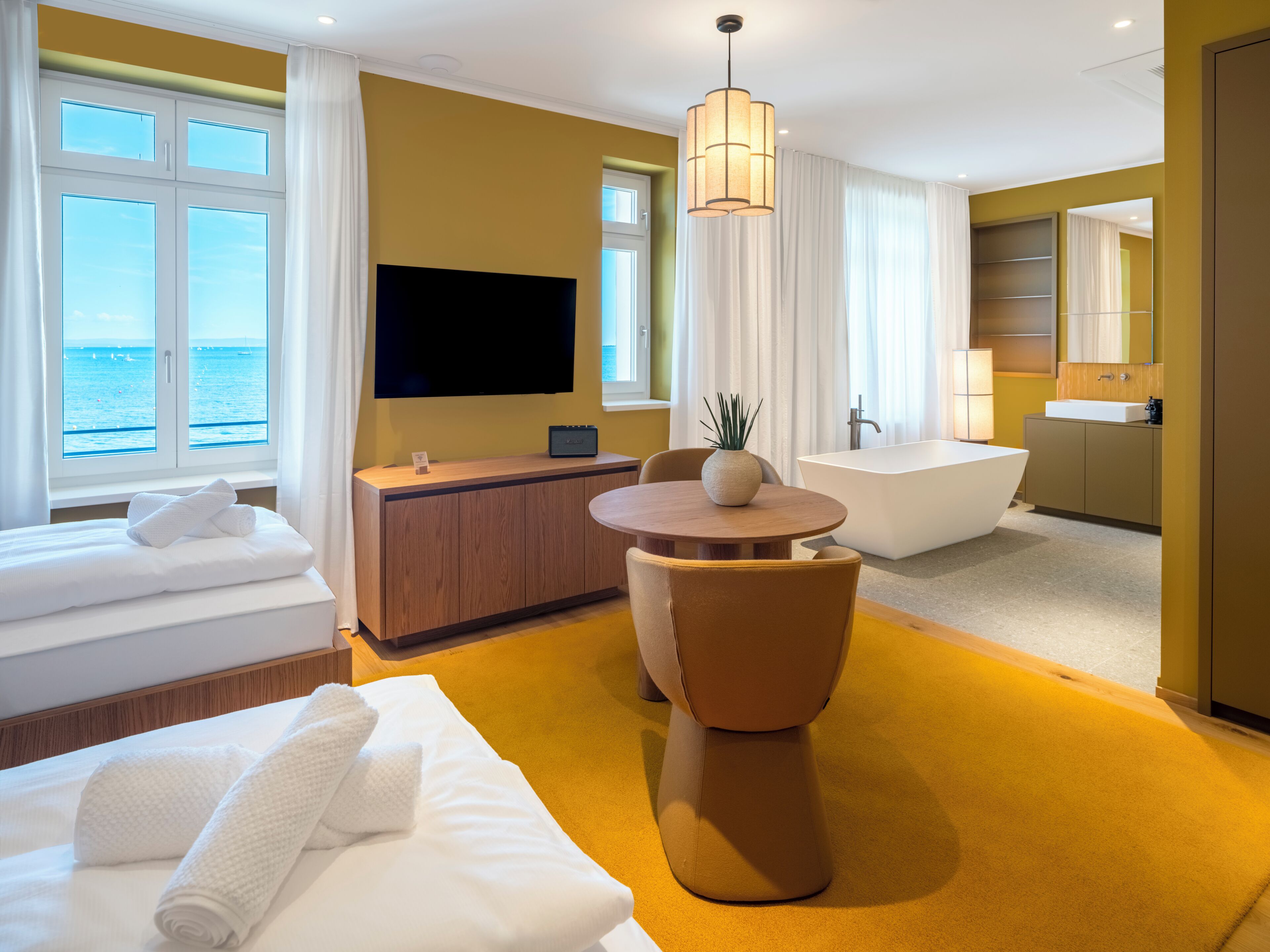 Habitación de hotel con cama, escritorio, televisor, bañera y vista al mar.