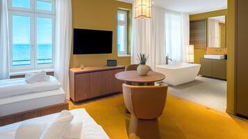 Habitación de hotel con cama, escritorio, televisor, bañera y vista al mar.