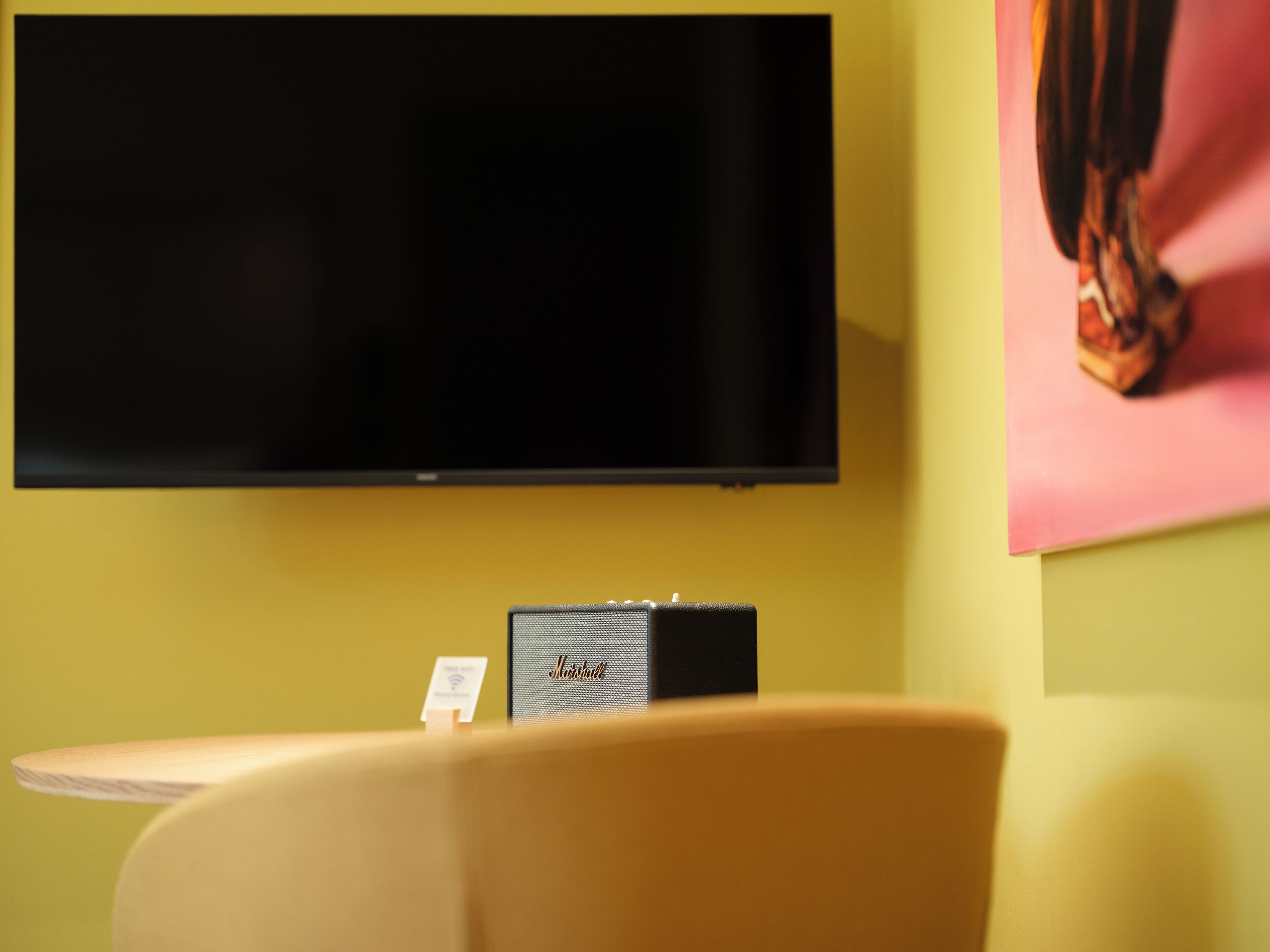 Una habitación con una televisión de pantalla plana montada en la pared, una pequeña mesa con una silla, y un cuadro enmarcado en la pared.