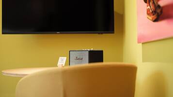 Una habitación con una televisión de pantalla plana montada en la pared, una pequeña mesa con una silla, y un cuadro enmarcado en la pared.