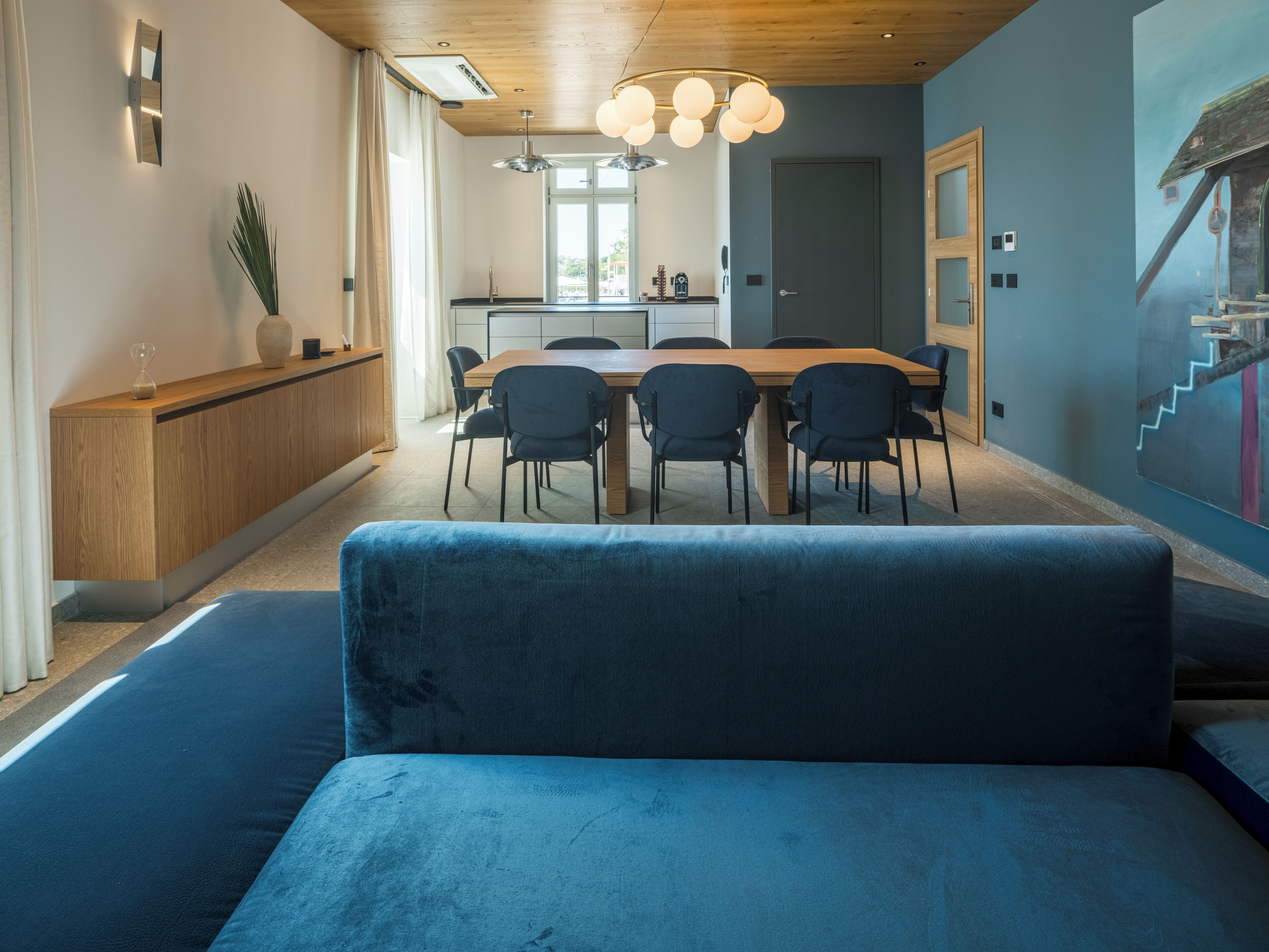 Un espace repas moderne avec une table en bois et des chaises noires, un canapé bleu au premier plan et une cuisine en arrière-plan.