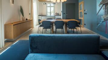 Un espace repas moderne avec une table en bois et des chaises noires, un canapé bleu au premier plan et une cuisine en arrière-plan.