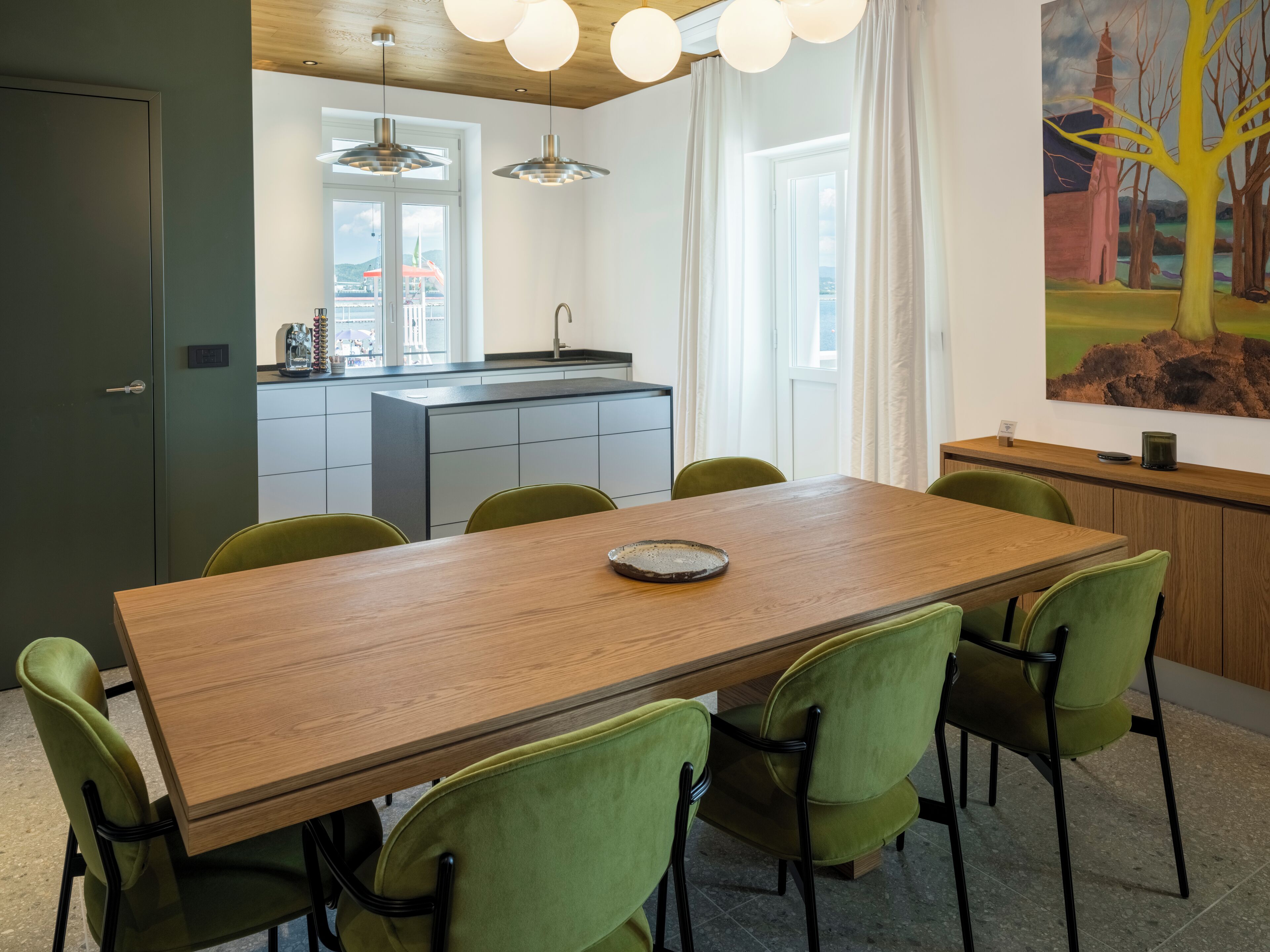 Una cocina moderna con una isla central, un comedor con mesa de madera y sillas verdes, y un cuadro en la pared.