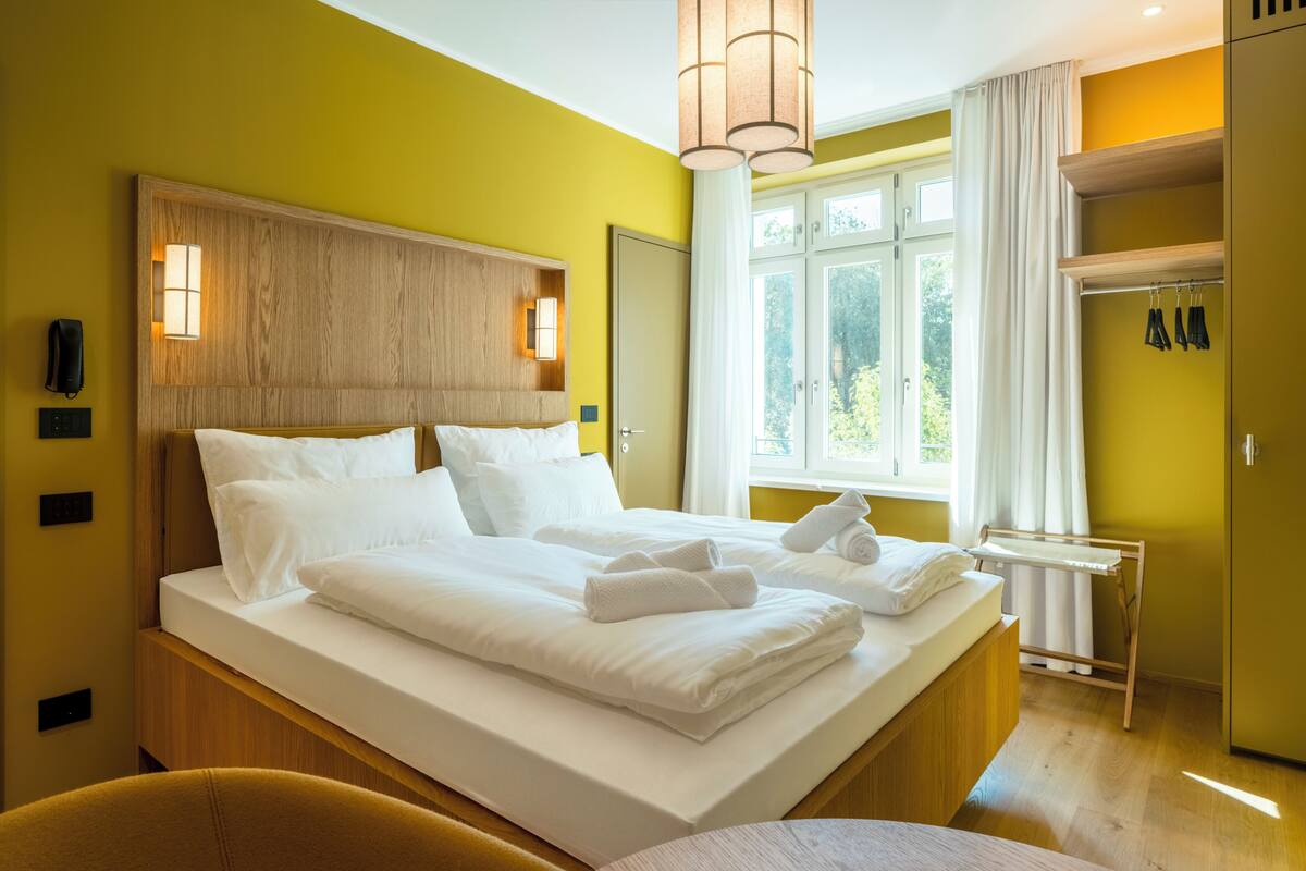 Ein Hotelzimmer mit einem großen Bett, Nachttischlampen, einem Fenster mit Vorhängen und einem Kleiderschrank.