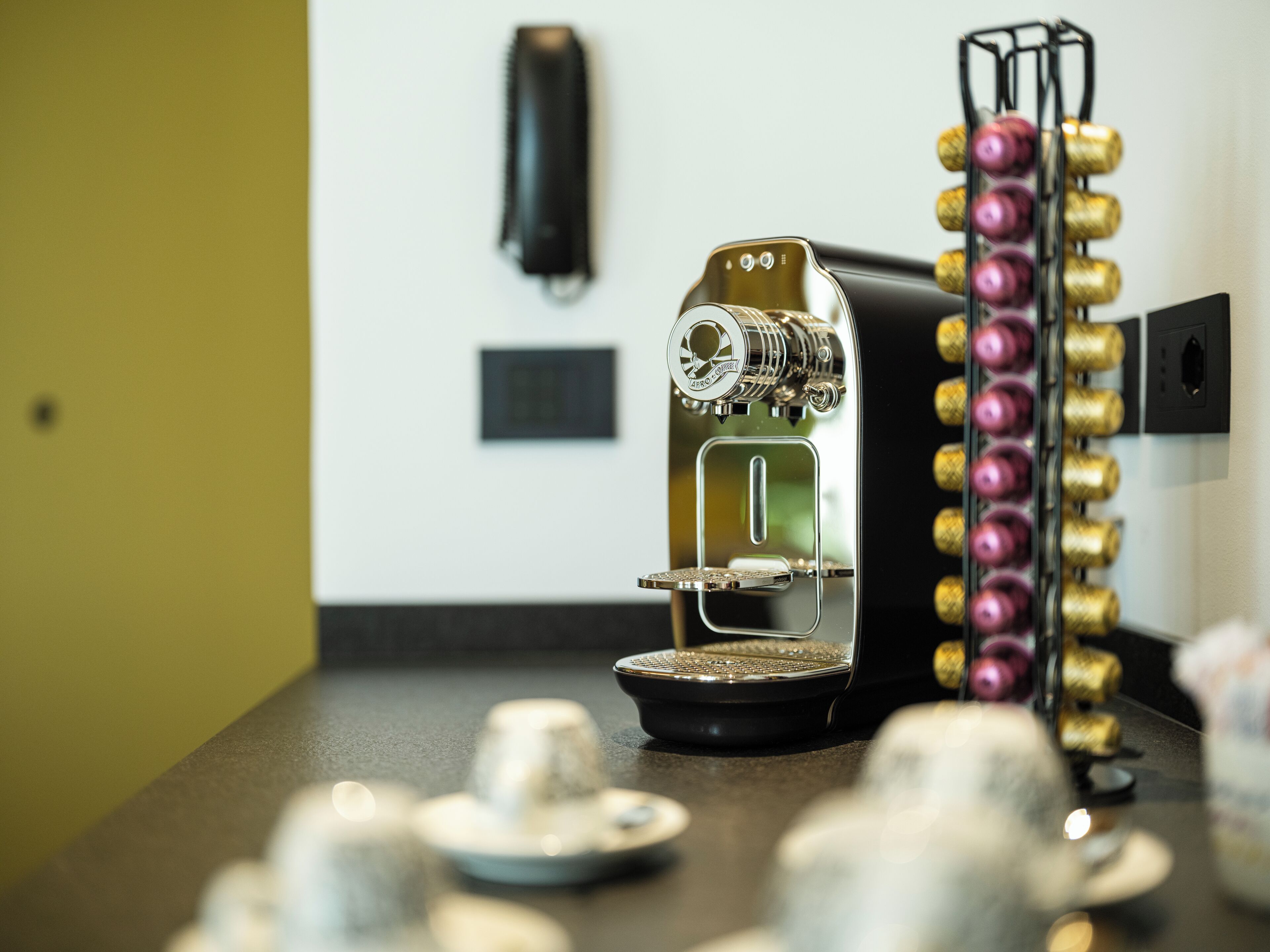 Eine Kaffeemaschine mit Metall- und Glasdesign, eine Kaffeemühle und eine Auswahl an Kaffeekapseln auf einer Arbeitsplatte.