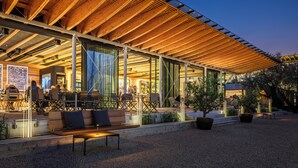 Un espace extérieur aménagé avec des bancs et des tables en bois, une terrasse couverte avec un toit en bois, et une vue sur le bar intérieur.