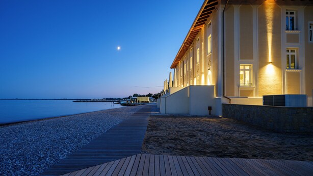 Un bâtiment situé sur la côte, doté d’une terrasse en bois et donnant sur une plage de galets.