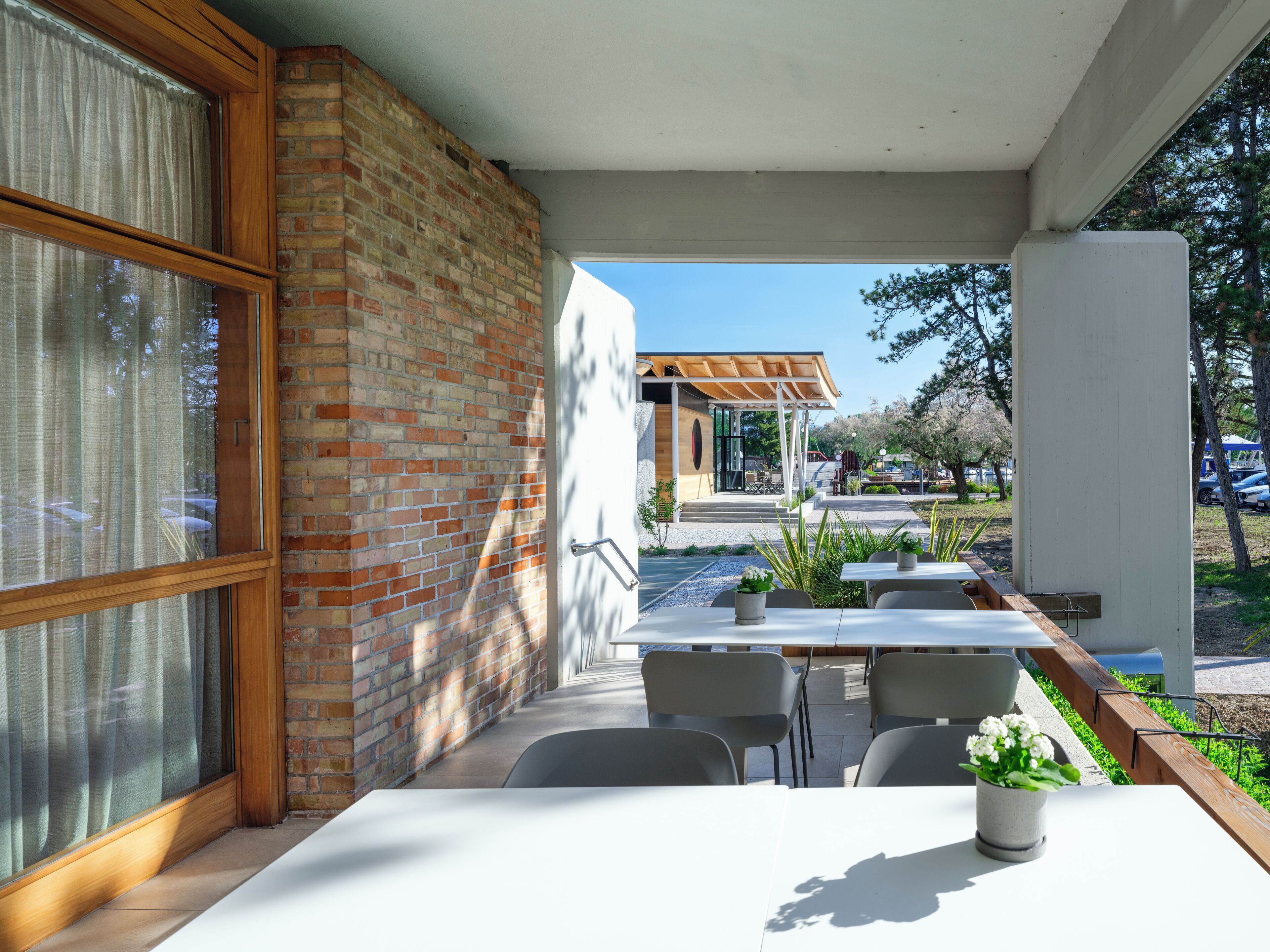 Un espace extérieur aménagé, abrité et doté de murs en briques, d’une pergola en bois et d’une vue sur un parking et des arbres.