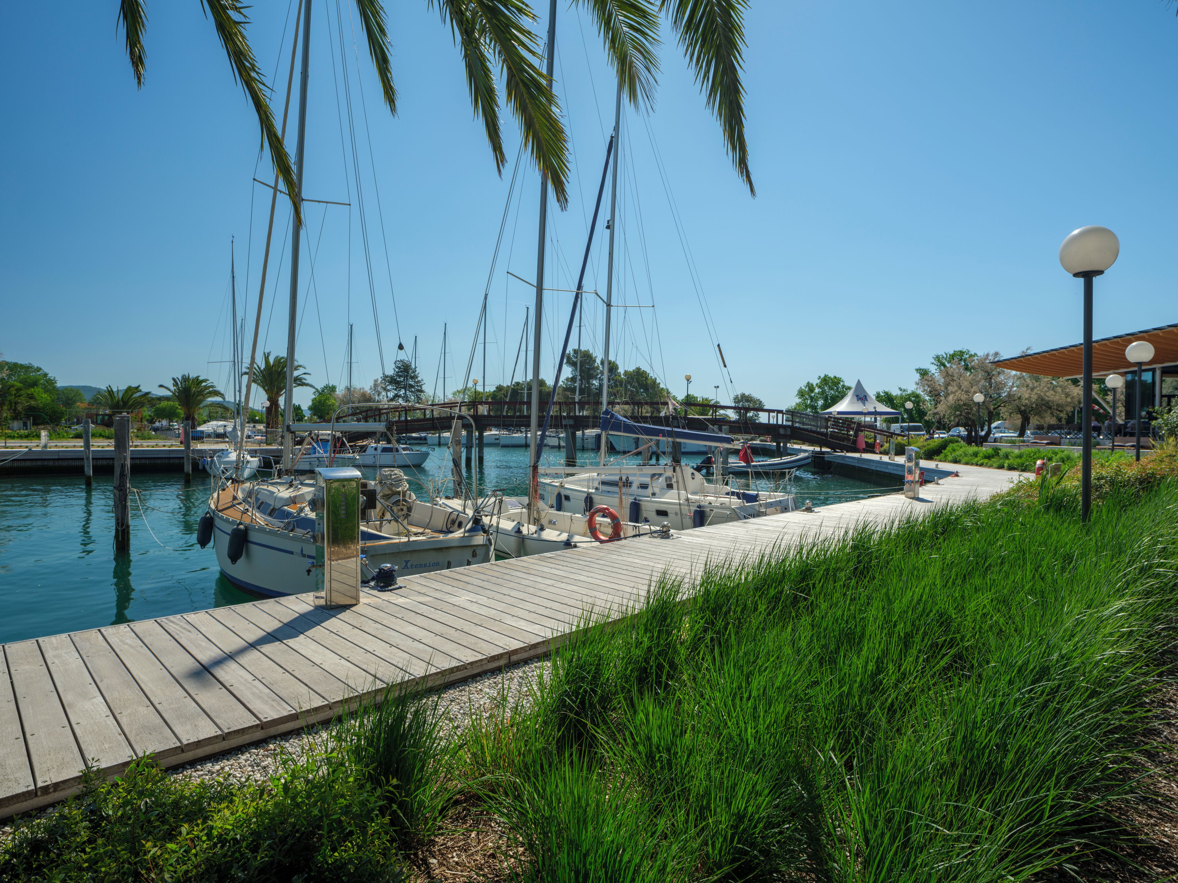 A marina with boats docked, a wooden walkway, and a bridge in the background.