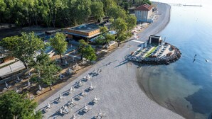 Une vue aérienne d’une propriété située en bord de mer, avec une rangée de chaises de plage et de parasols, un bâtiment doté d’un toit rouge et une côte rocheuse.