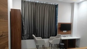 A hotel room with a bed, a desk, two chairs, a TV, and a window with curtains. - Hotel Kamboj (Kharar)