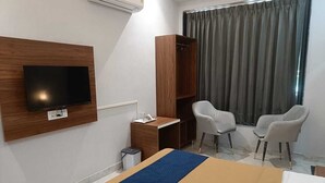 A hotel room with a bed, a TV mounted on the wall, a desk with a chair, and a wardrobe. - Hotel Kamboj (Kharar)