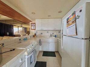Una cocina compacta con armarios blancos, horno integrado, refrigerador y ventana con vistas panorámicas.