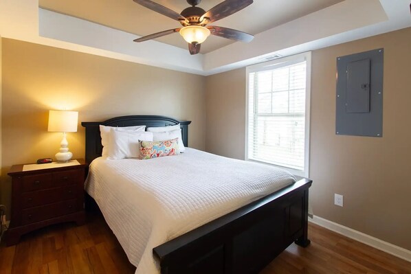 Une chambre à coucher avec un lit, une table de chevet, une lampe, un ventilateur de plafond et une fenêtre.