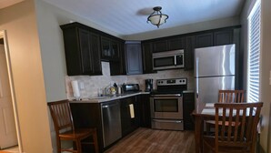 Una cocina con armarios oscuros, electrodomésticos de acero inoxidable, una mesa de comedor de madera y sillas.