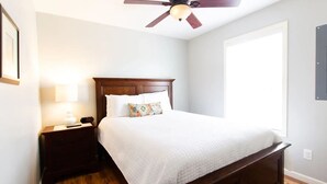 Une chambre à coucher avec un lit en bois, une table de chevet, une lampe et un ventilateur de plafond.