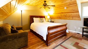 Ein Schlafzimmer mit Holzboden, einem Bett mit weißer Bettdecke, einem Nachttisch mit Lampe, einem Holzstuhl und einem Fernseher.