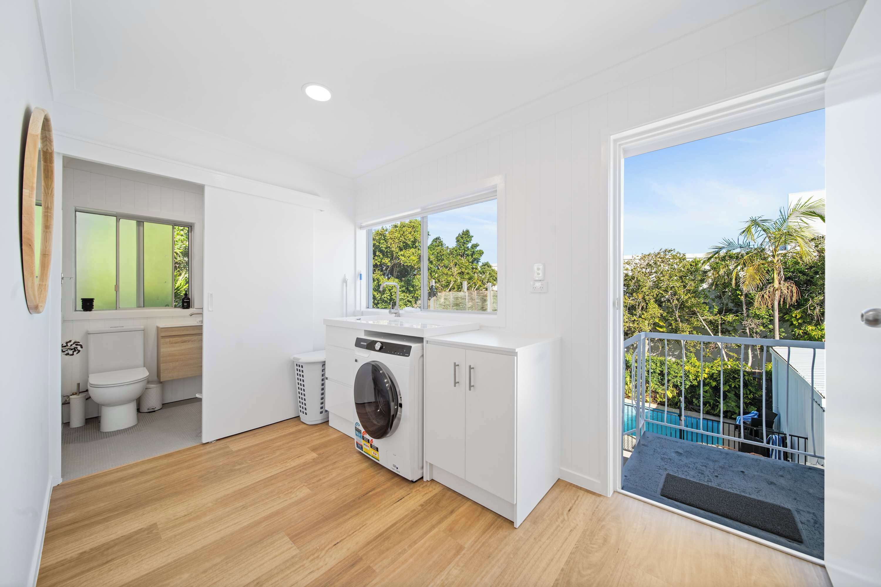 Un apartamento pequeño con zona de lavandería, un inodoro y un balcón con vistas al verdor.