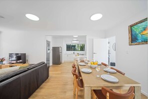 Une cuisine moderne avec des meubles blancs, une table à manger pour quatre personnes et une grande fenêtre.