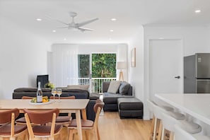 Un soggiorno moderno con zona pranzo, divano, cucina e balcone con vista sul verde.