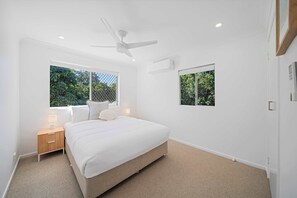 A bedroom with a bed, two bedside tables, a ceiling fan, and two windows.