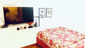 Een slaapkamer met een televisie, een bed met een bloemenbedekking en twee ingelijste foto's aan de muur.