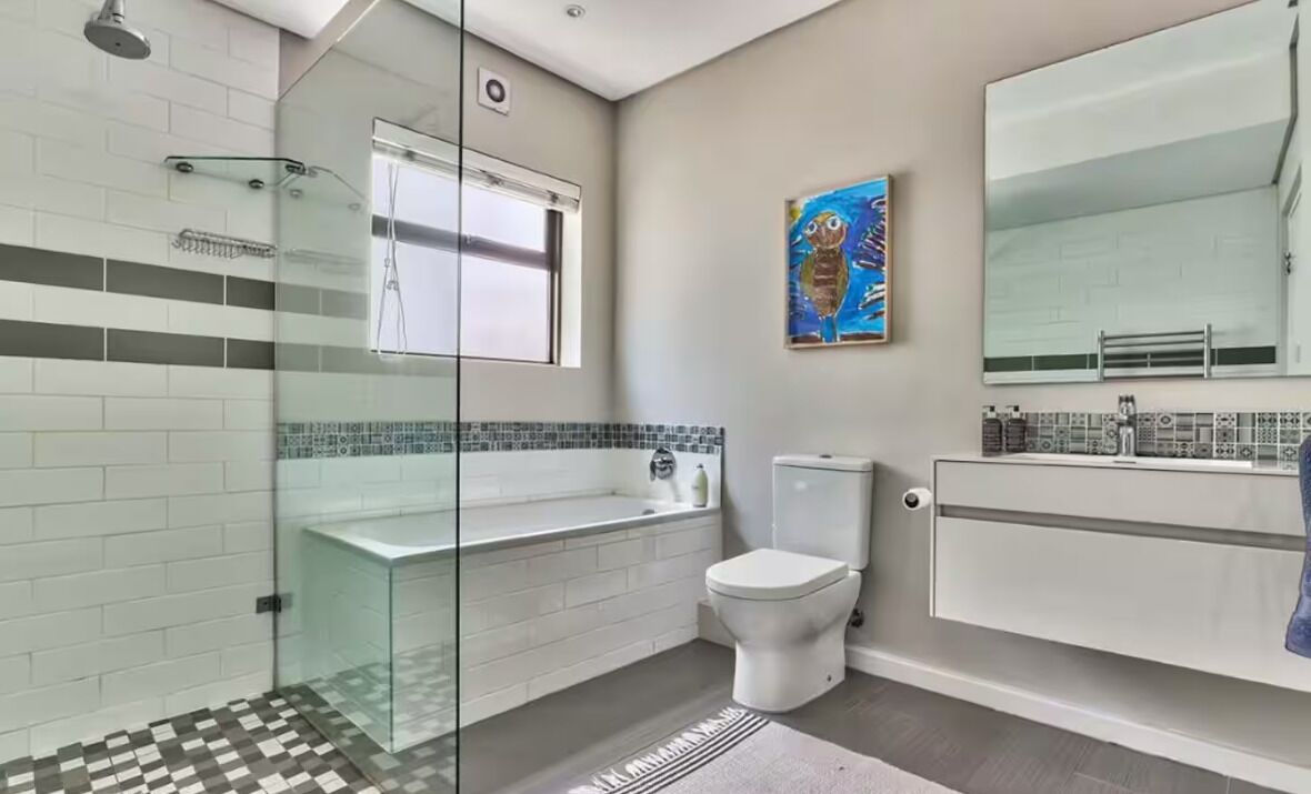 Een moderne badkamer met een douchecabine van glas, een wit toilet en een grote spiegel boven de wastafel.