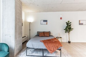 A modern bedroom with a bed, a bedside table, a floor lamp, a potted plant, and a large window. - 2  New Studios with Stunning City Views (Cleveland)